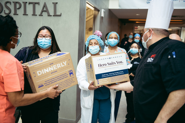 Two health care workers in face masks receive Dinnerly meal kits from hospital staff.